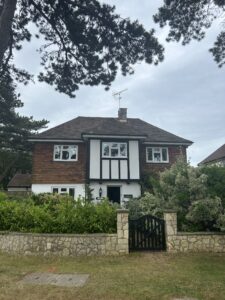 Detached double fronted house with shrubs in the front garden, a low wall and wooden front gate.