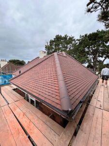 View from scaffolding of a ridged new roof fitted with flat brick coloured tiles and a ridge with clay tiles
