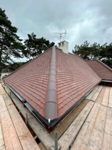 View from scaffolding of a ridged new roof fitted with flat brick coloured tiles and a ridge with clay tiles