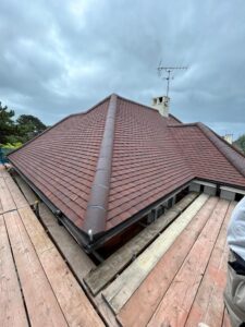 View from scaffolding of a ridged new roof fitted with flat brick coloured tiles and a ridge with clay tiles