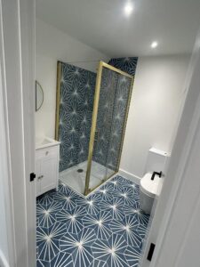 Refurbished shower room with white painted walls, brass shower cubicle and blue and white tiles fitted to the floor and inside the cubicle.