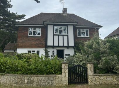 Detached double fronted house with shrubs in the front garden, a low wall and wooden front gate.