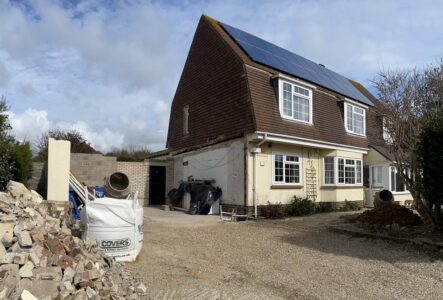 Detached house shown before a new side extension has been built. Builders rubble shown in the foreground as well as concrete mixer.