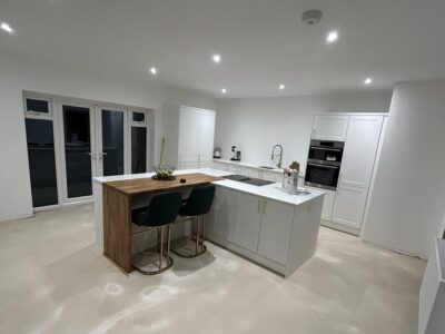 New kitchen fitted in a house extension with white units, central island, recessed lighting and breakfast bar. French doors led out to the garden.