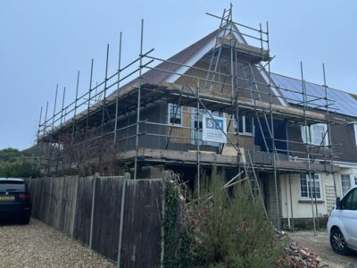 Work in progress for a two storey side extension for a large detached house. Scaffolding covers the new construction which has a timber frame and white UPVC windows.