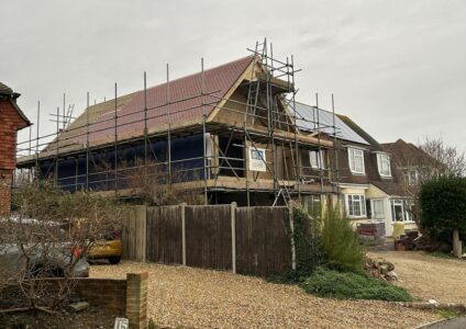 Work in progress for a two storey side extension for a large detached house. Scaffolding covers the new construction which has a timber frame and partly-tiled roof.