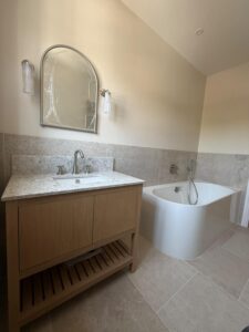 Bathroom with curved bath, wood vanity unit with marble top and arched mirror.