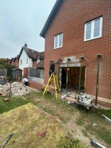 Rear view of a brick built house with workman creating an opening to the garden.
