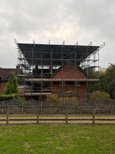 External view of house being extended with scaffolding covering the rear extension and roof